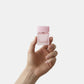 Hand holding a small pink bottle against a light gray background