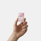 Hand holding a small pink bottle against a light gray background