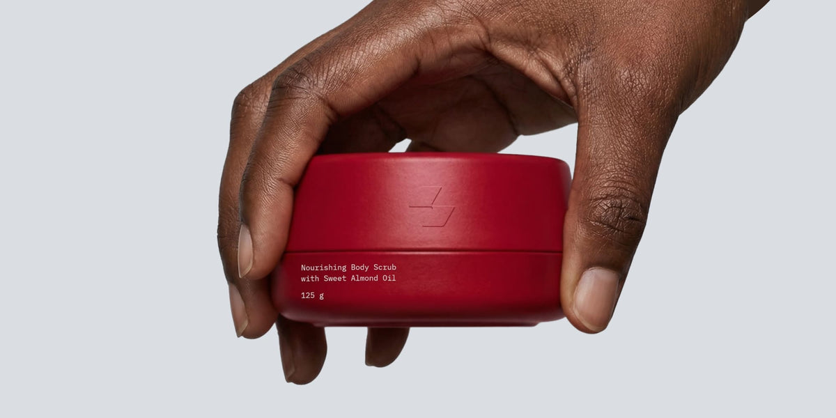 Hand holding red nourishing body scrub container with sweet almond oil