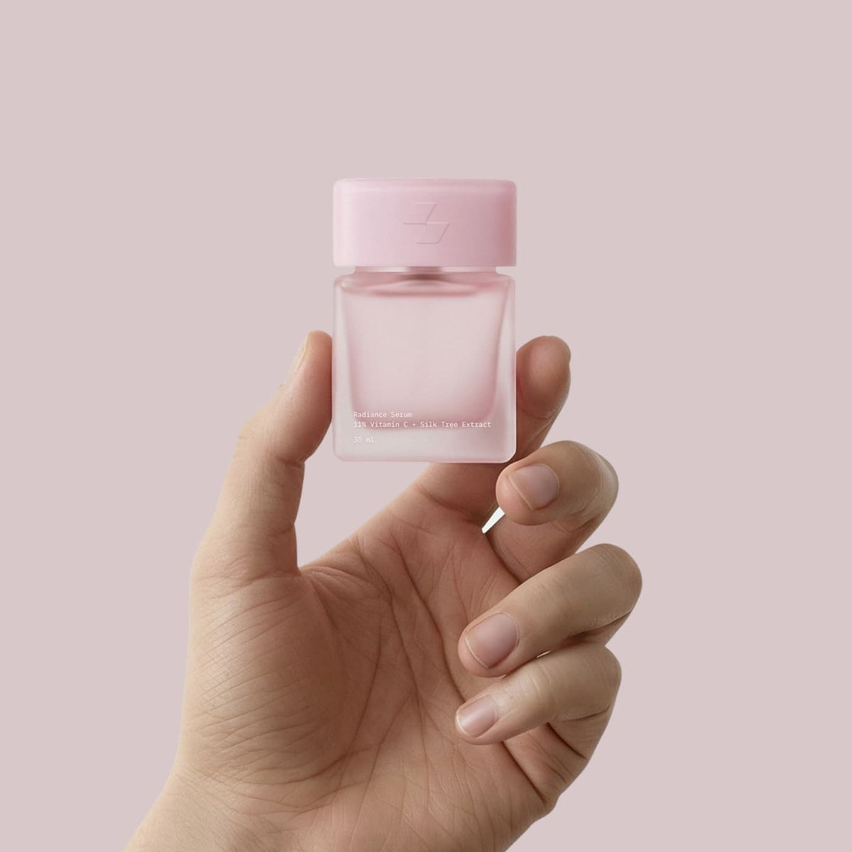 Hand holding pink radiance serum bottle with vitamin C and silk tree extract
