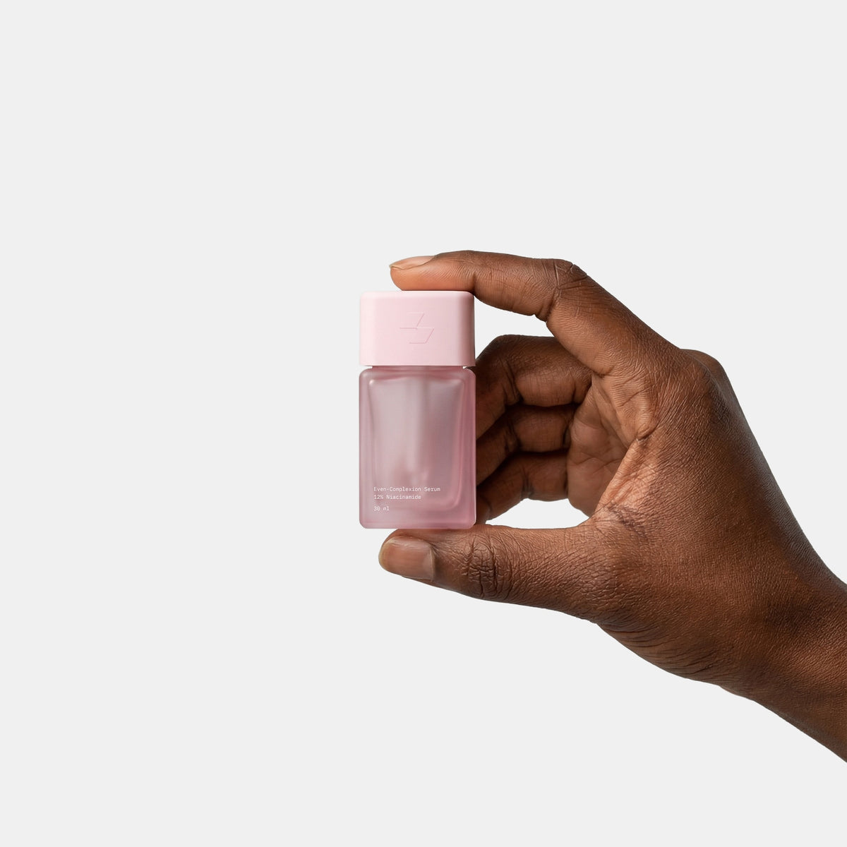 Hand holding a small pink bottle against a light gray background
