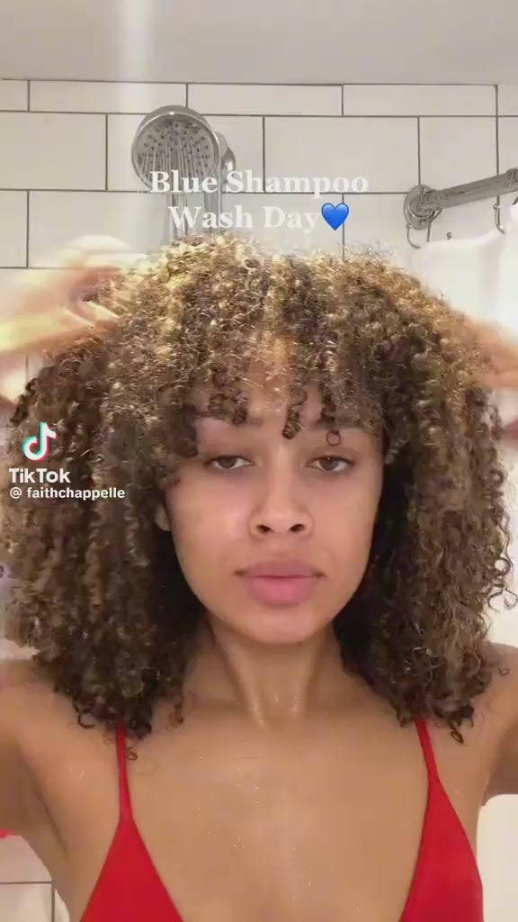 Woman with curly hair washing with blue shampoo under shower during wash day