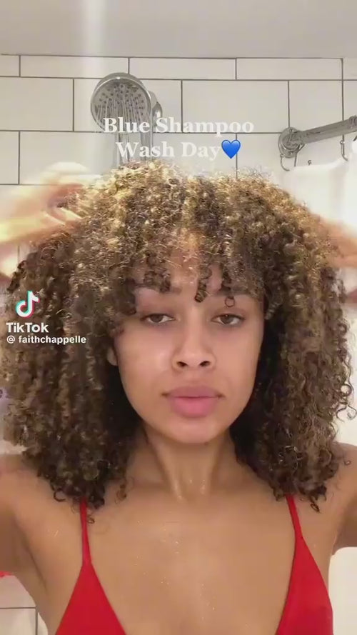 Woman with curly hair washing with blue shampoo under shower during wash day