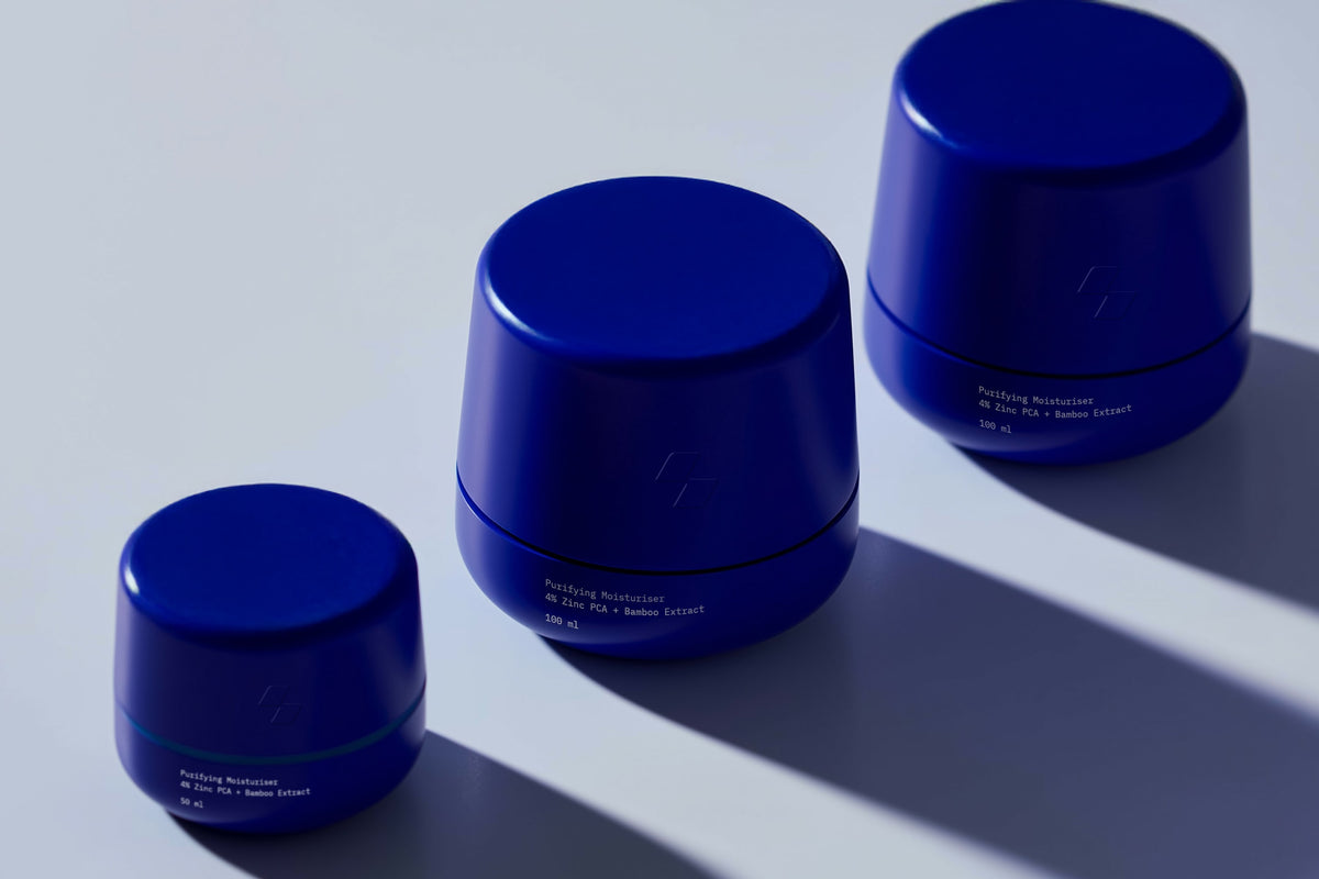 Three blue cosmetic jars on a reflective surface with a light gray background
