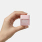 Hand holding a small pink container against a light gray background
