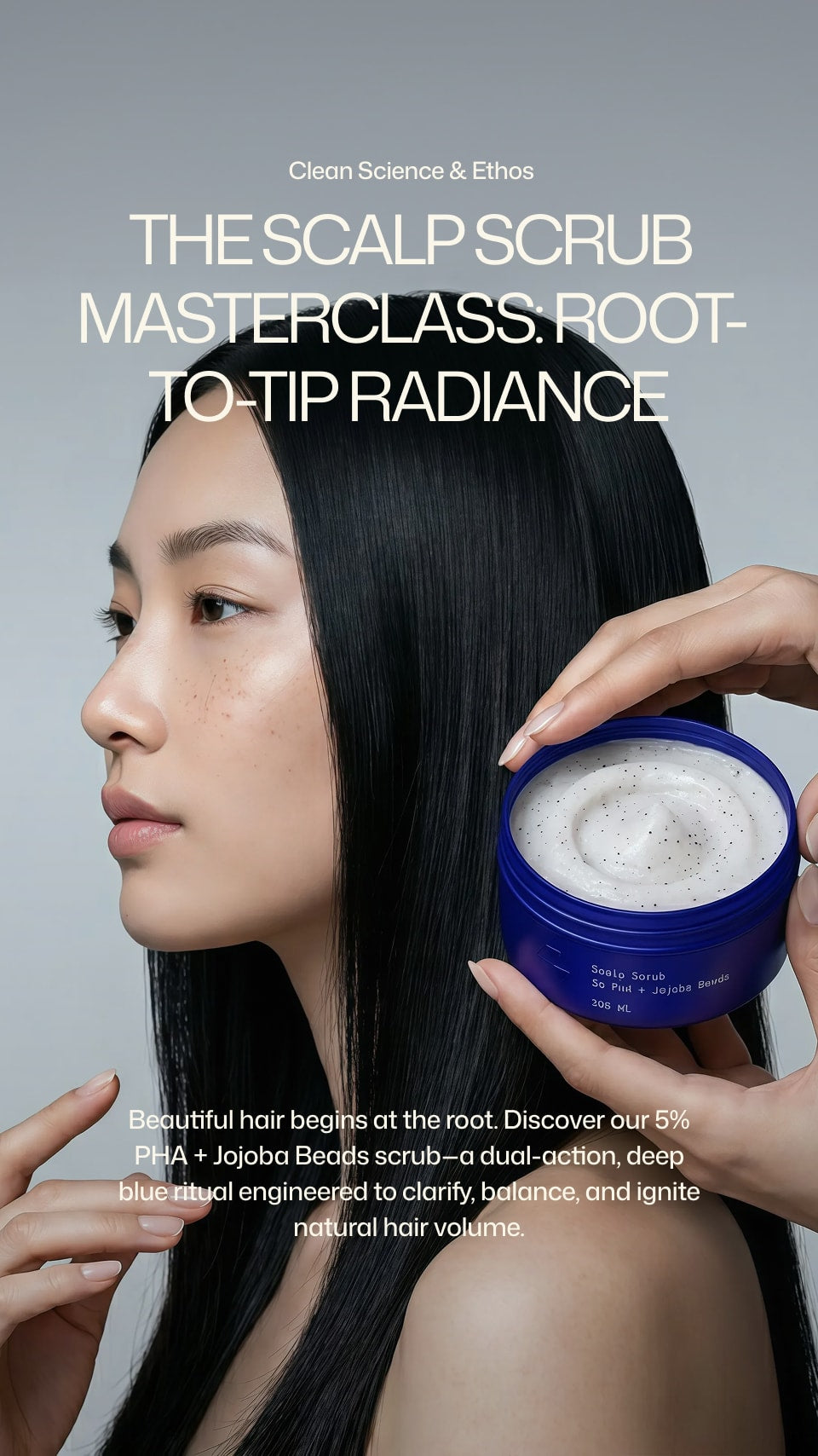 Woman with long black hair holding a scalp scrub jar against a gray background